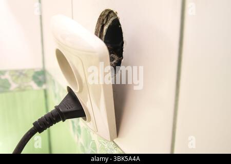 Eine defekte Steckdose in einem Haus oder Apartment weist auf die Gefahr hin, dass eine freiliegende Steckdose repariert werden muss. Eine gefährliche gebrochene Steckbuchse in einem Stockfoto