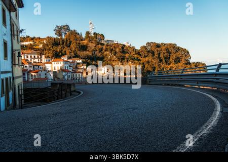 Küstendorf auf einem Hügel gelegen, von einer gewundenen Straße aus gesehen. Lastres, Asturien Stockfoto