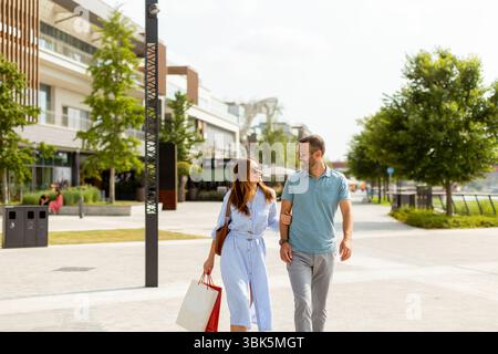 Ein fröhliches Paar spaziert Hand in Hand, erkundet charmante Geschäfte, während es an einem schönen Tag im Freien das warme Sonnenlicht genießt. Stockfoto