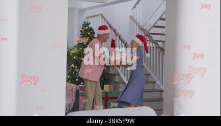 Tanzendes Paar mit Weihnachtsmützen im Flur, Weihnachtsbaum, Geschenke und Girlanden-Geländer Stockfoto
