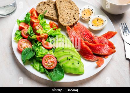 Gesunde ausgewogene Frühstücks- oder Mittagstisch - hart gekochtes Ei, Vollkorntoast, Lachs, Avocado und grüner Gemüsesalat. Ausgewogene Diätmahlzeit von protei Stockfoto