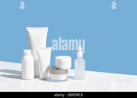 Behälter für Kosmetikprodukte auf weißem und blauem Hintergrund, Kopierraum. Weiße leere Feuchtigkeitspflege für das Gesicht, Reinigungsgel-Tube, Körperlotion, Gesichtsserum b Stockfoto