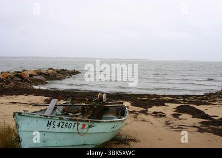 Ein verwittertes Ruderboot sitzt verlassen an einem mit Algen bedeckten Strand unter grauem Himmel in der Küste von Massachusetts. Stockfoto