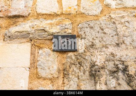 Alte Hausnummer an einer strukturierten Steinmauer. Vintage-Schilder, urbane Textur und architektonische Details in mediterranen Dörfern. Stockfoto