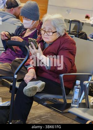 Ältere grauhaarige asiatische Frau liest auf ihrem Handy. Erstellt 05.20.25 Stockfoto
