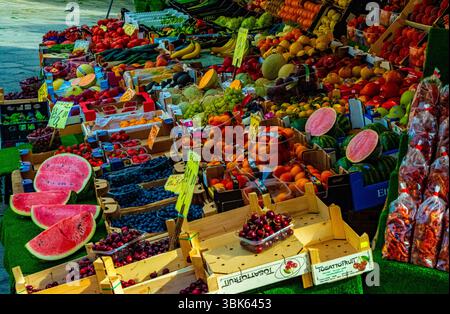 Venedig, Italien – 15. Juni 2025: Verschiedene frische Früchte, darunter Wassermelonen, Kirschen, Bananen und Beeren, werden auf einem traditionellen Markt im Freien präsentiert Stockfoto
