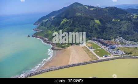 Aus der Vogelperspektive fängt die atemberaubende Küstenschönheit von orio, spanien, mit dem Strand, dem türkisfarbenen Wasser, den üppigen grünen Bergen, und die pulsierende Stadt Stockfoto