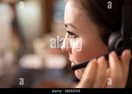 Kaukasischer Kundendienstspezialist mit freihändigen Headsets, der sich auf technische Unterstützung konzentriert. Nahaufnahme einer jungen Mitarbeiterin, die ihren Kopfhörer berührt, während sie einem externen Kunden zuhört. Stockfoto