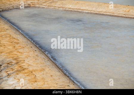 Ein detaillierter Blick auf eine einzelne Saline, die in den frühen Stadien der Verdunstung in einer traditionellen Salzwasserplatte mit Meerwasser gefüllt ist. Stockfoto