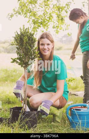 Porträt einer lächelnden kaukasischen jungen Frau, die einen kleinen Baum im Garten pflanzt Stockfoto