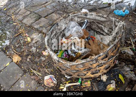 Bali, Indonesien - 25. Dezember 2024: Dreckiger Korb voller Müll liegt auf dem Boden. Der Müll enthält viele Plastikflaschen und ein paar Dosen. Der Korb ist Stockfoto