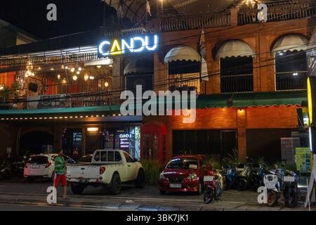 Bali, Indonesien - 25. Dezember 2024: Das Restaurant CANDU ist nachts beleuchtet. Das Gebäude ist gemauert und hat eine grüne Markise. Es gibt mehrere geparkte Autos Stockfoto