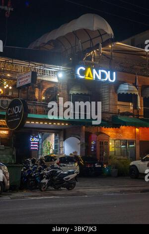 Bali, Indonesien - 25. Dezember 2024: Das Restaurant CANDU ist nachts beleuchtet. Das Gebäude ist gemauert und hat eine grüne Markise. Es gibt mehrere geparkte Autos Stockfoto