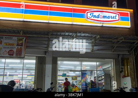 Bali, Indonesien - 25. Dezember 2024: Mädchen spazieren vor dem Indomaret-Supermarkt. Die Straße ist dunkel. Stockfoto