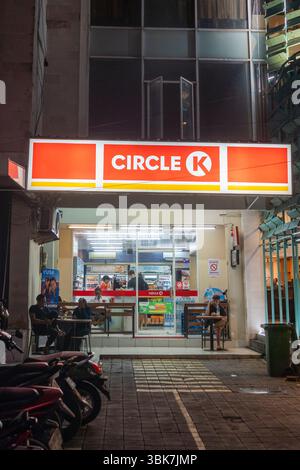 Bali, Indonesien - 25. Dezember 2024: Mann sitzt vor dem Indomaret-Supermarkt. Die Straße ist dunkel. Stockfoto