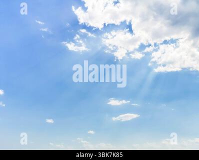 Hellblauer Himmel mit weichen weißen Wolken und Sonnenstrahlen, die durchströmen, schaffen eine ruhige und friedliche Atmosphäre, perfekt für Hintergründe oder Natur Stockfoto