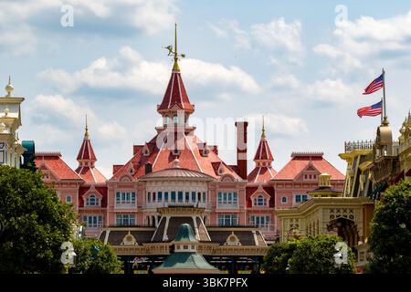 Rosafarbenes und rotes Gebäude mit Türmen und Türmen vor einem blauen und bewölkten Himmel, aus einem niedrigen Winkel mit Bäumen im Vordergrund im Disneyland Paris, Stockfoto