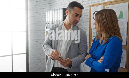 Geschäftsmann und Geschäftsfrau diskutieren über die Arbeit in einem modernen Büroumfeld, während er Informationen auf einem Mobiltelefon unter professionellen Diagrammen und Dokumenten zeigt Stockfoto