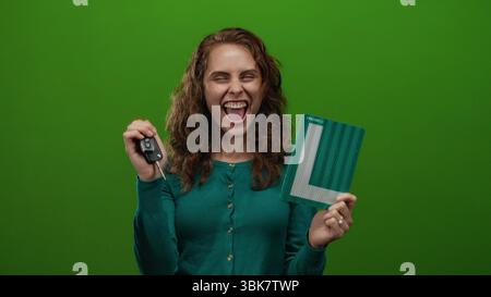 Frau, die mit Freude und Aufregung Autoschlüssel und Lernzeichen vor isoliertem grünem Hintergrund hält. Stockfoto