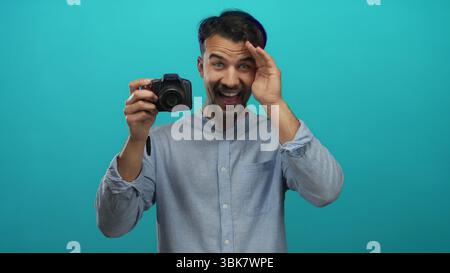 Junger Mann mit Kamera über isoliertem blauem Hintergrund, der Fotos in kreativer Fotoszene aufnimmt. Stockfoto
