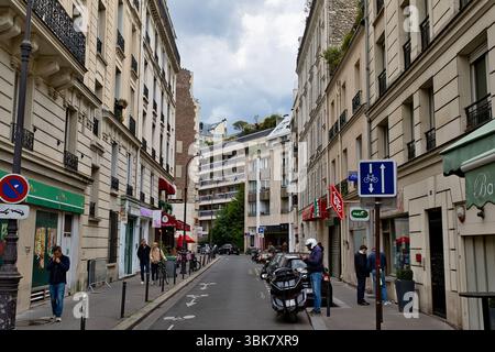 Blick auf die Straße in Paris, mit Gebäuden, geparkten Fahrzeugen, Fußgängern und Straßenschildern an einem bewölkten Tag. Stockfoto