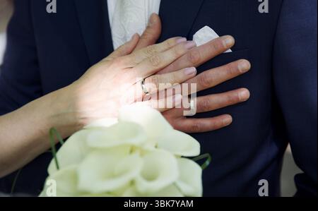 Nahaufnahme der Hände von Braut und Bräutigam mit Ringen und Blumen Stockfoto