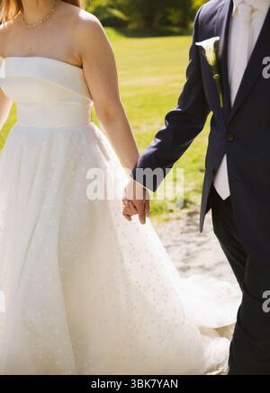 Nahaufnahme von Braut und Bräutigam, die Hände halten und draußen gehen Stockfoto