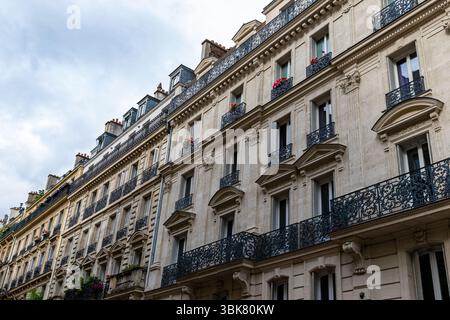 Niedrigwinkelaufnahme von Pariser Gebäuden mit verzierten Balkonen, Fenstern und architektonischen Details unter einem bewölkten Himmel. Stockfoto