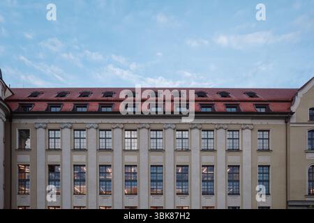 Ein symmetrischer Blick auf eine historische Gebäudefassade mit zahlreichen Fenstern über mehrere Etagen, gekrönt von einem markanten roten Fliesendach mit mehreren Stockfoto