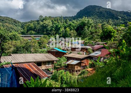 Rustikales Holzdorf in tropischer Berglandschaft, eingebettet in dichten grünen Wald. Traditionelle Pfahlhäuser mit Metalldächern unter stimmungsvollem Himmel, rur Stockfoto