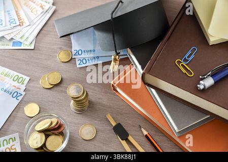 Bildungsausgabekonzept mit Mörtelplatte auf Bücherstapel und Geld auf Holztisch. Draufsicht. Stockfoto