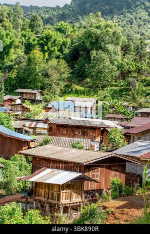 Traditionelles Bergstamm Dorf umgeben von üppigem Regenwald im Norden Thailands. Hölzerne Pfahlhäuser unter tropischem Vordach in einem friedlichen Berg va Stockfoto