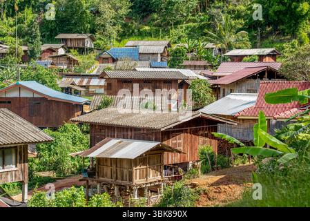 Nahaufnahme eines traditionellen thailändischen Dorfes mit Holzpfahlhäusern und Metalldächern, umgeben von tropischer Vegetation und grünen Hügeln im Norden Th Stockfoto