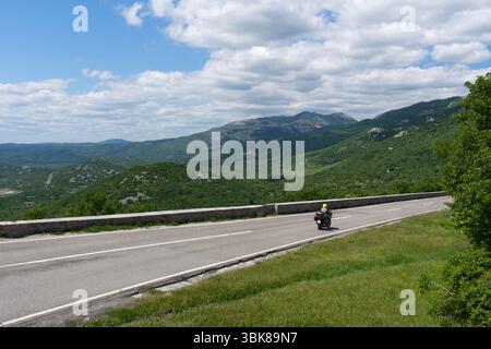Ein Motorrad fährt auf einer gewundenen Straße durch üppige grüne Berge unter einem hellen, bewölkten Himmel und zeigt eine malerische Reise. Stockfoto