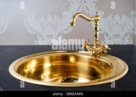 Luxuriöse Küche mit rundem Waschbecken aus goldenem Messing und Armatur mit Doppelhahn in zeitgenössischem, modernem Design mit Steingut-Steingut-Co aus Steinmarmor Stockfoto