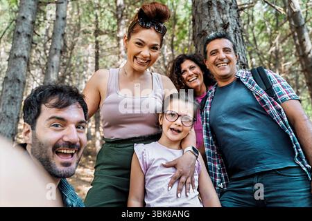 Eine große, glückliche und vielfältige Gruppe von Freunden oder Familie lacht während einer Wanderung im Wald, während sie zusammen mit einem Smartphone ein Selfie macht Stockfoto