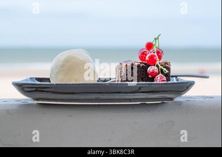 Auf einem wunderschön angeordneten Teller sitzt ein köstlicher Brownie, begleitet von einer großzügigen Portion cremigem Eis Stockfoto