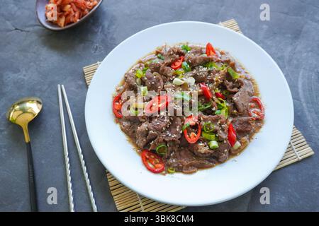 Bulgogi ist ein koreanisches Gericht, das aus Rindfleisch mit Sauce und Gewürzen gegrillt wird. Auf schwarzem Hintergrund Stockfoto