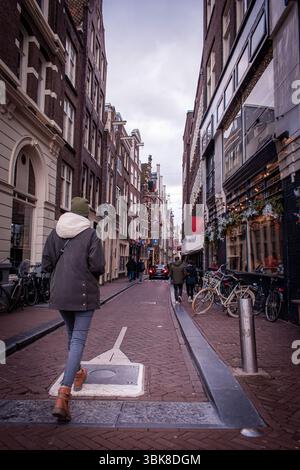 Ein Mädchen spaziert durch die Straßen Amsterdams, gesäumt von wunderschönen, farbenfrohen Häusern, verschiedenen Cafés und Pubs, mit Fahrrädern auf dem Weg. Stockfoto