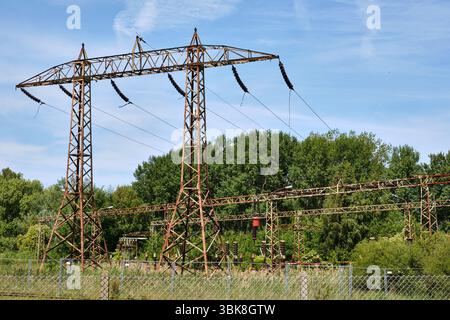 Alte verrostete Hochspannungsmasten und Isolatoren am stillgelegten Kraftwerksstandort in der Nähe von Peenemünde, umgeben von Bäumen und bewachsener Vegetation. Stockfoto