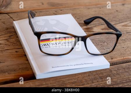 Grundgesetz der Bundesrepublik Deutschland mit Brille 19.06.25, Limburg: Symbolfoto, Illustrationsbild, Symbolbild, Illustrationsfoto, Alltagsszene eine Brille liegt auf einem geschlossenen Exemplar des Grundgesetzes der Bundesrepublik Deutschland. Das Buch mit Bundesadler und schwarz-rot-goldenem Streifen liegt auf einem Holztisch. Die Szene steht symbolisch für reflektiertes Lesen, politische Bildung, Rechtsbewusstsein und den individuellen Zugang zu demokratischen Werten und Grundrechten. Limburg *** Grundgesetz der Bundesrepublik Deutschland mit Brille 19 06 25, Limburger Symbolbild, Stockfoto
