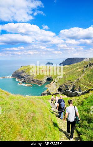 Touristen wandern entlang der dramatischen Küste am Tintagel Castle auf dem South West Coast Path mit Blick auf die Klippen und Barras Nose, Cornwall UK Stockfoto