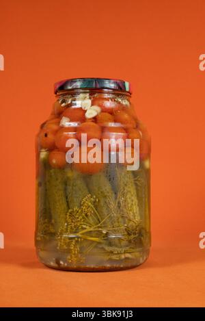Hausgemachte eingelegte Dosentomaten und Gurken in einem Glas auf einem leuchtend orangen Hintergrund Stockfoto