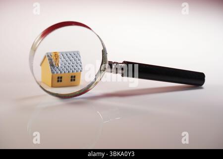 Nahaufnahme der Lupe auf dem kleinen Puppenhaus vor weißem Hintergrund Stockfoto