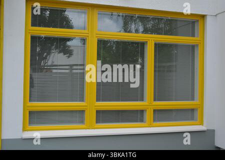 Dinge Objekte, Haus mit gelber Fassade, Wohnung mit Rasen. Große gelbe Kunststofffenster mit eingebauten weißen Jalousien. Stockfoto