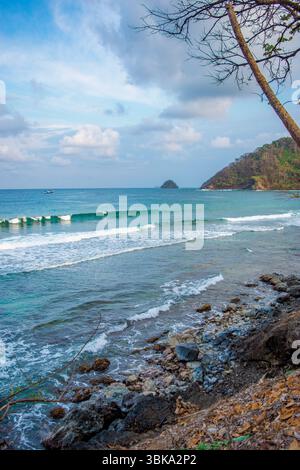 Atemberaubende Küstenlandschaft von Sapzurro, Choco, Kolumbien mit sanften Wellen, felsigen Küsten und üppigem Grün unter einem dramatischen Himmel. Stockfoto