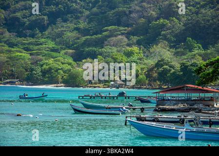 Ein ruhiger Blick auf den Strand Sapzurro in Choco, Kolumbien, mit farbenfrohen Booten auf klarem türkisfarbenem Wasser, umgeben von üppigen grünen Hügeln. Stockfoto