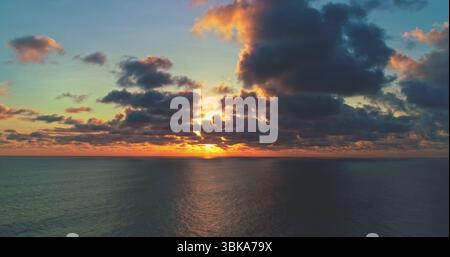 Aus der Vogelperspektive erblicken Sie einen atemberaubenden Sonnenuntergang über einem ruhigen Ozean, mit leuchtenden Farben, die den Himmel bemalen, und dunklen Wolken, die der Meereslandschaft einen Hauch von Drama verleihen Stockfoto