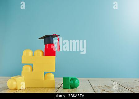 Mehrfarbige Konstruktionswürfel für Kinder und schwarze und Masters-Kappe oder oxford-Kappe auf blauem Hintergrund. Konzeptbildung, Entwicklung und Stockfoto