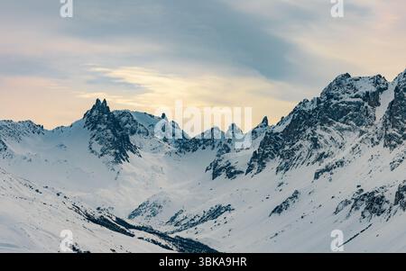 Schneebedecktes Bergtal mit felsigen Gipfeln bei Sonnenuntergang Stockfoto